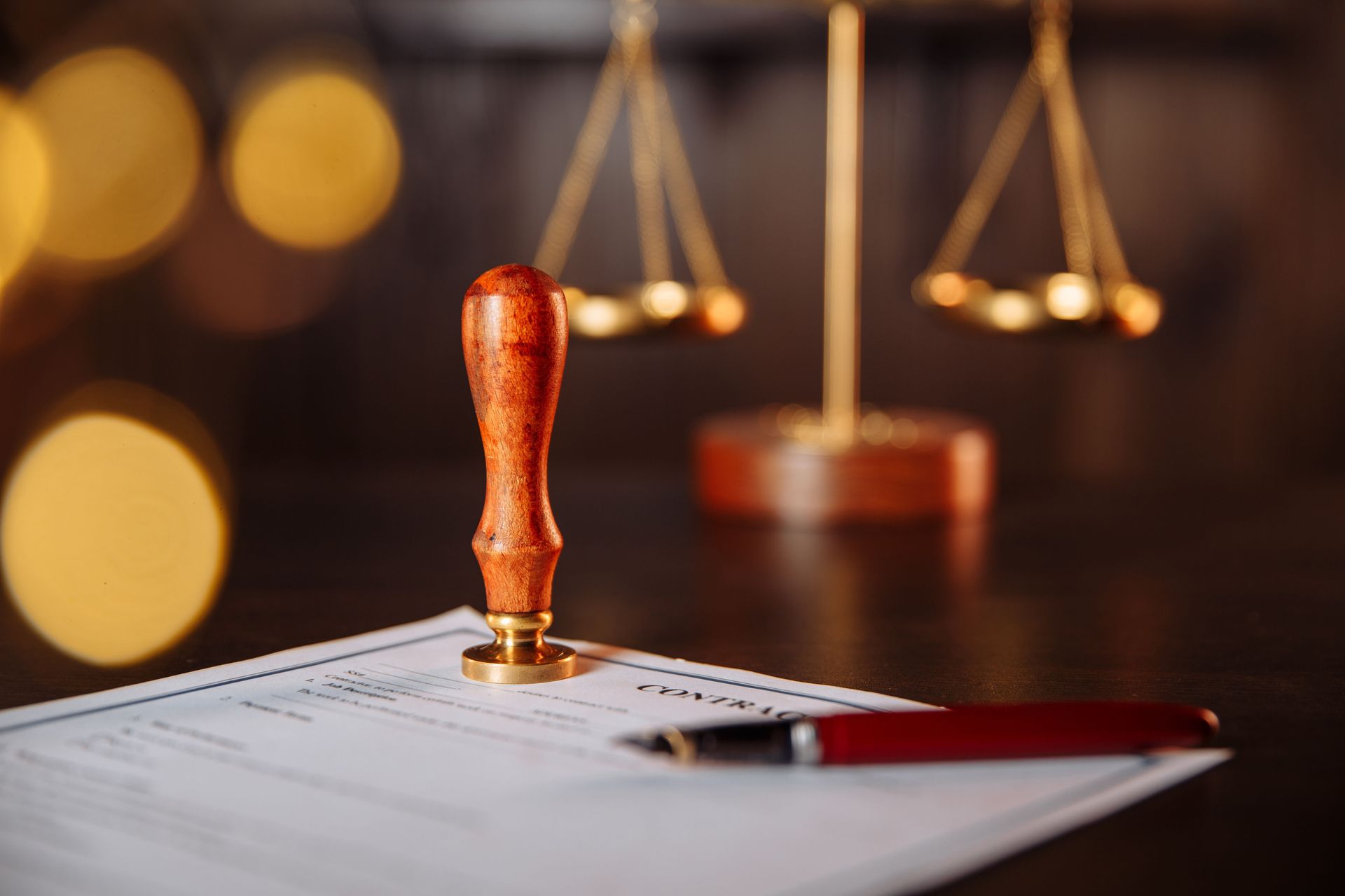 Scales of justice, notary stamp, and pen on a document, in a blurred setting with warm light.