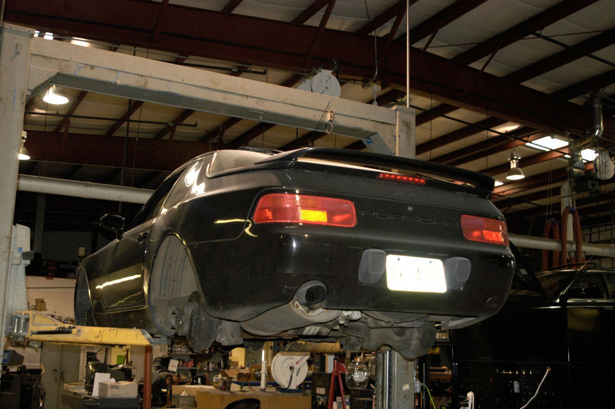 A black sports car elevated on a hydraulic lift inside an auto repair shop.