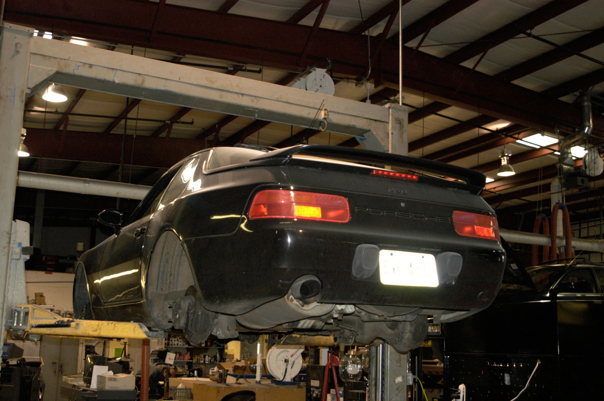 A black sports car elevated on a hydraulic lift inside an auto repair shop.
