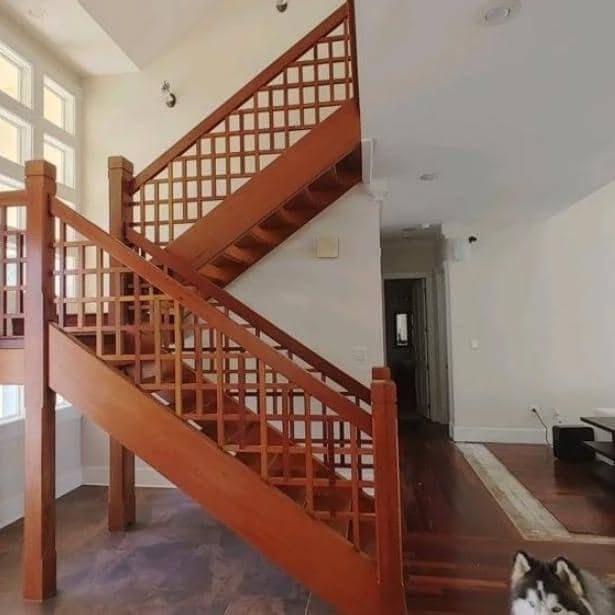 Wooden staircase with a lattice design, leading to a second floor. A husky dog is at the bottom.