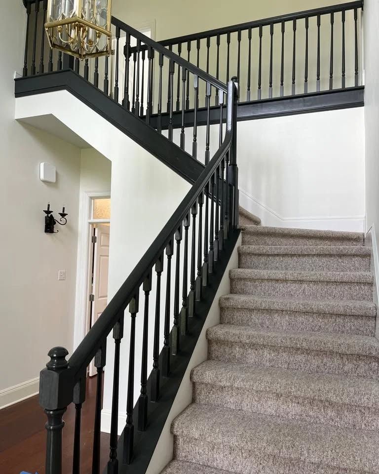 Staircase with black railings and carpeted steps. The walls are white and the entry has a chandelier.