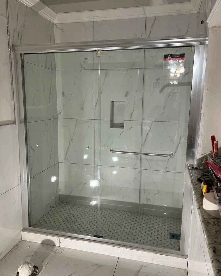Glass shower enclosure with sliding door and marble-patterned tile.
