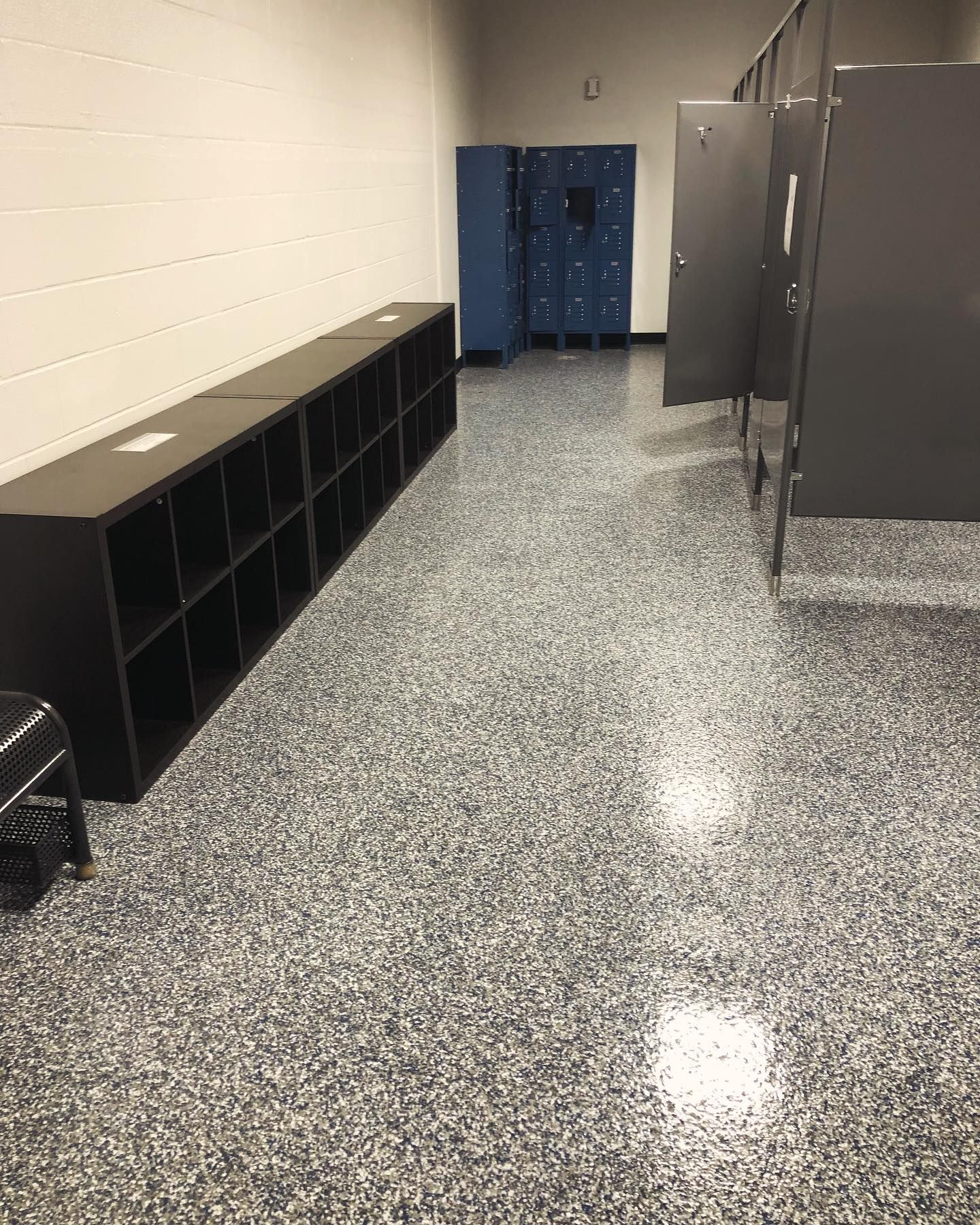 A locker room with black cubby shelves, blue lockers, and dark gray stall doors. The floor is speckled.