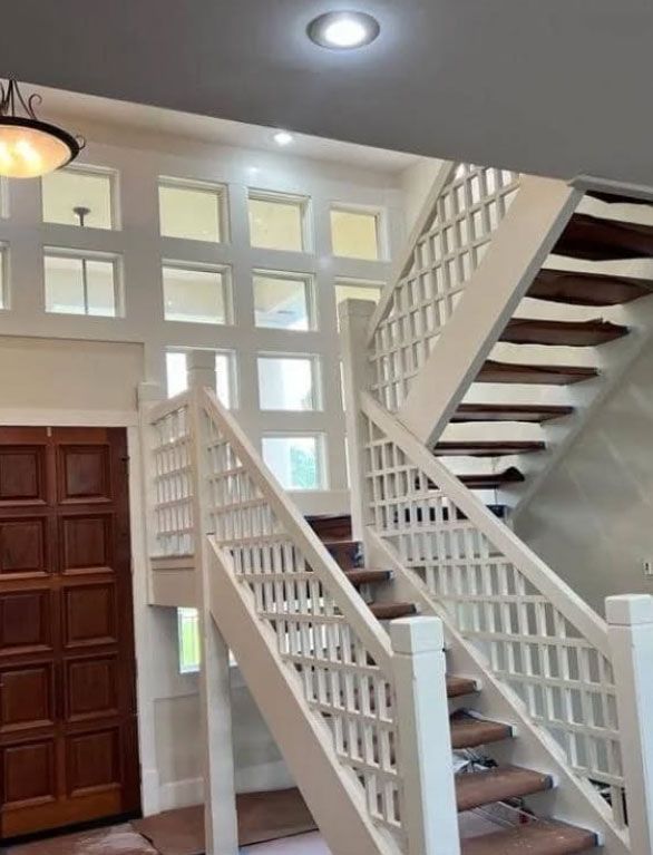 Two-story entry hall with white latticed staircase, brown wooden door, and square windows.