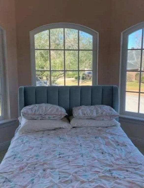 A bed with a blue headboard in front of a window, covered in a floral comforter and pillows.