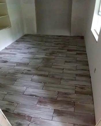 Empty room with wood-look tile flooring. Two alcoves and a window are visible; walls are white.