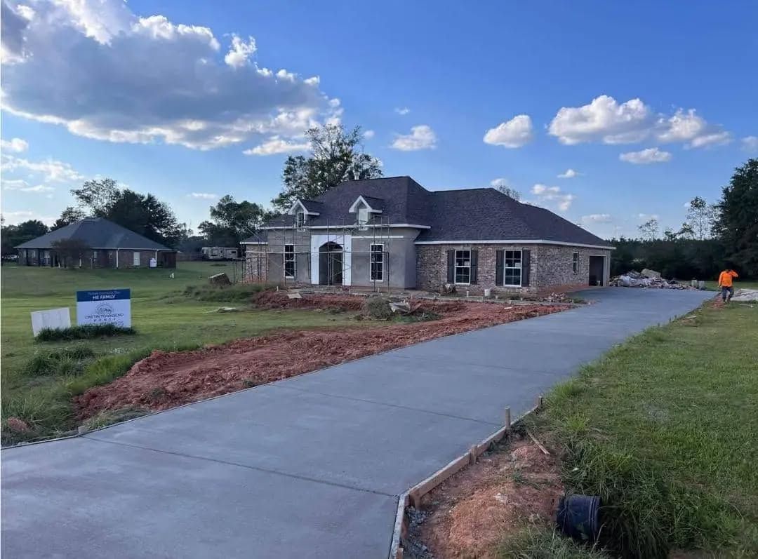 Newly constructed brick home with long concrete driveway, blue sky.