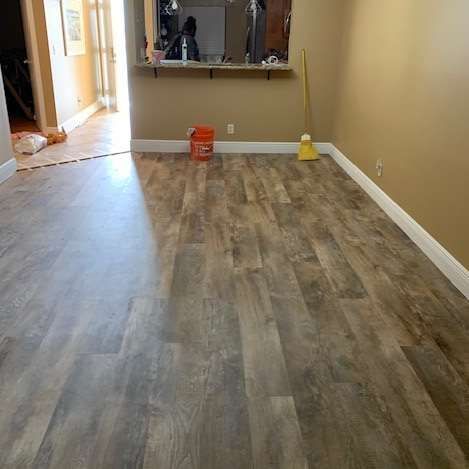 Room with wood-look flooring, tan walls, and a small counter opening. A broom and bucket are visible.
