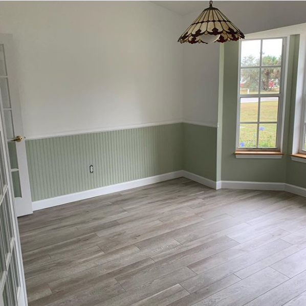 Empty room with wood-look flooring, green wainscoting, and white upper walls. A window and hanging light fixture are visible.
