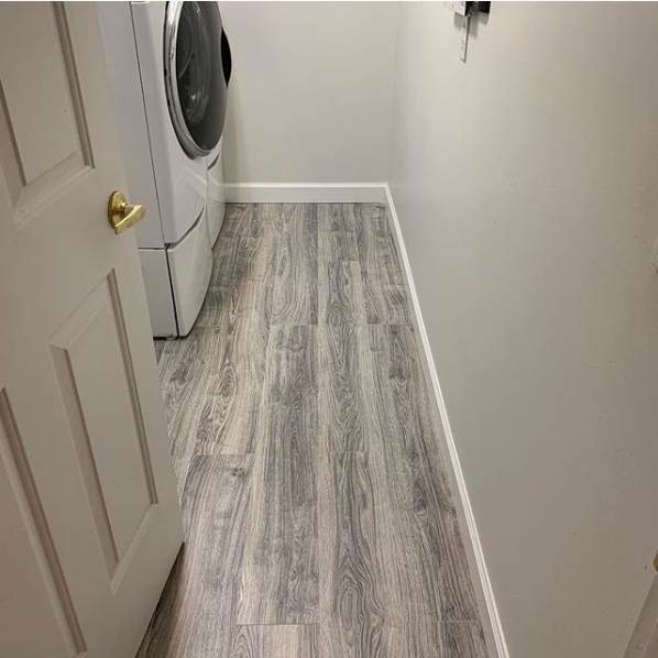 Laundry room with gray wood-look flooring, white washer and dryer, white door, and white trim.