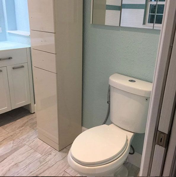 Bathroom with white toilet, tall cabinet, pale blue wall, and light-colored tile floor.