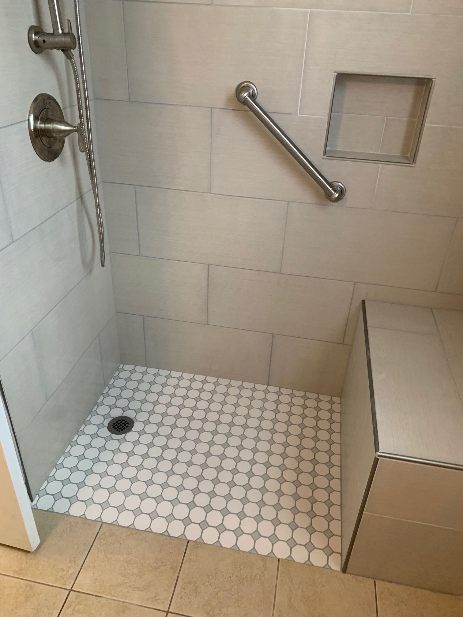 Bathroom shower with tiled walls and floor, built-in seat, grab bar, and recessed shelf.