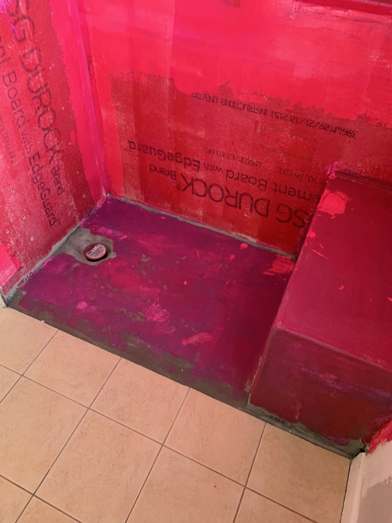 Shower stall under construction, featuring red waterproofing membrane, drain, and tiled floor.