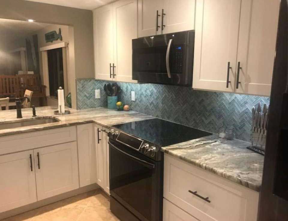 White kitchen cabinets, black appliances, granite countertops, and blue tile backsplash.