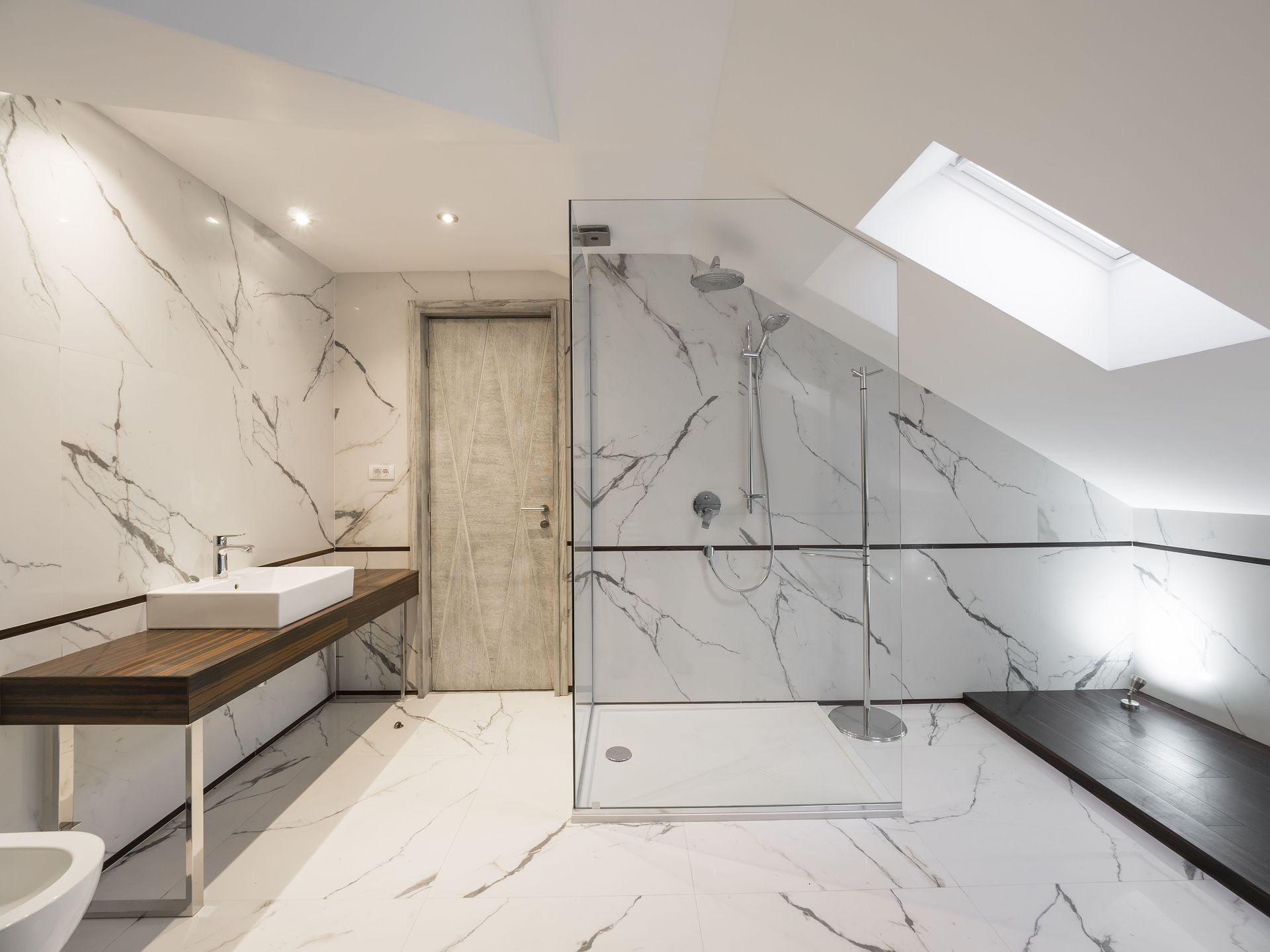Modern bathroom with marble-look walls, glass shower, wooden vanity, and skylight.