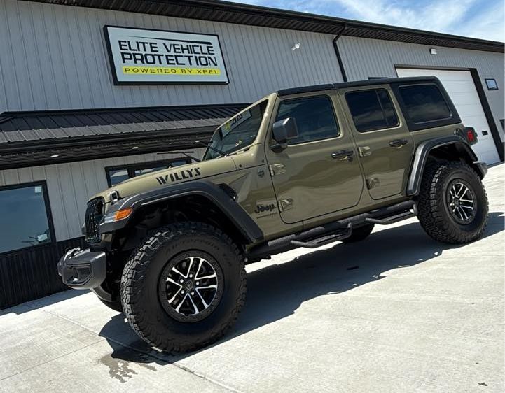 A green jeep wrangler is parked in front of a building.