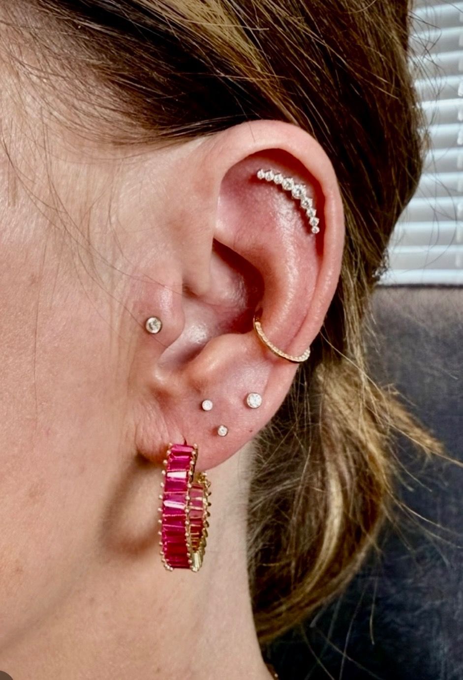 Woman's ear with multiple piercings, including a helix and lobe earrings. Gold and pink jewels.