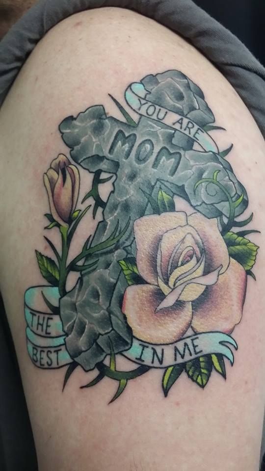 A tattoo of a cross with roses and a banner that says
