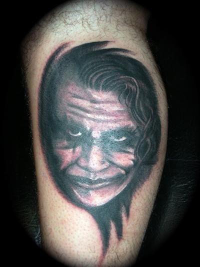A man has a tattoo of the joker on his leg.
