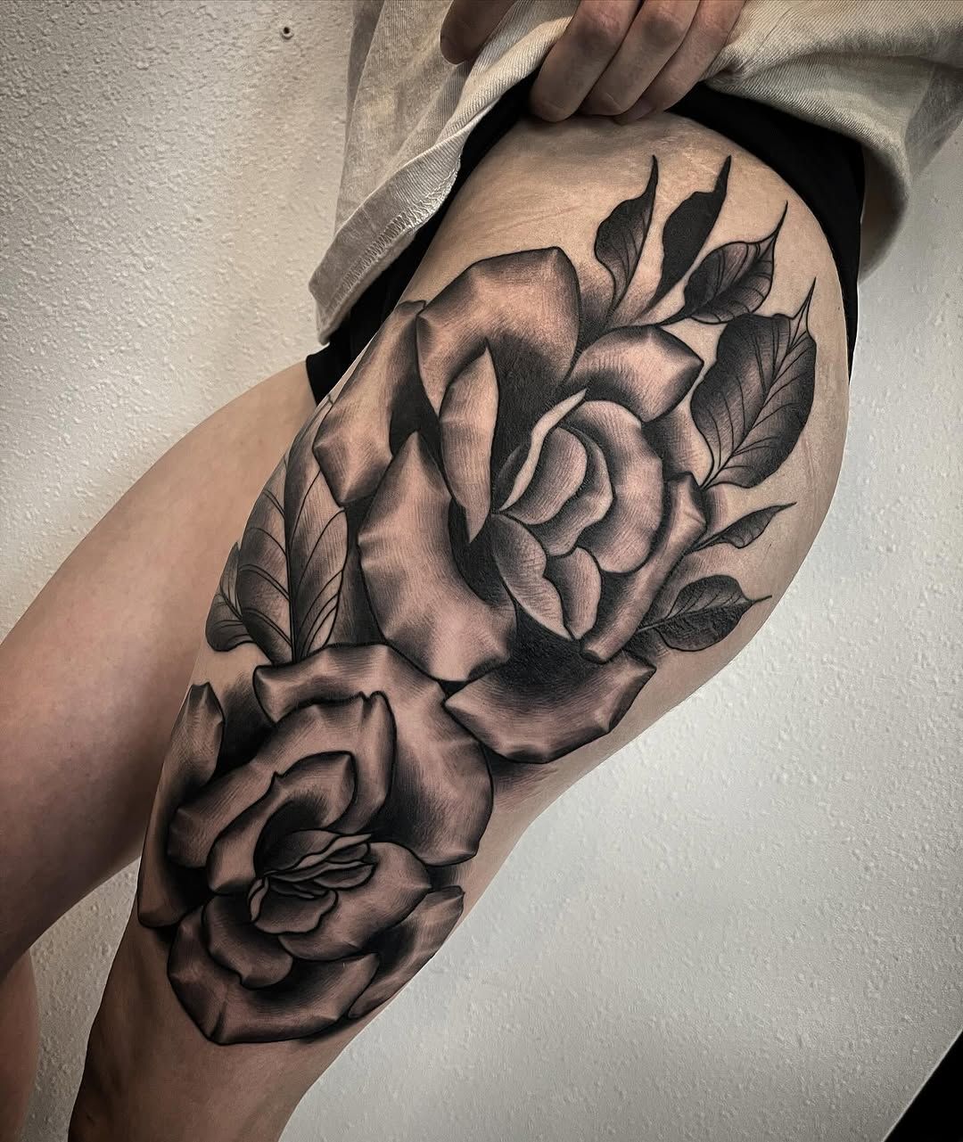 A woman has a black and white tattoo of two roses on her thigh.