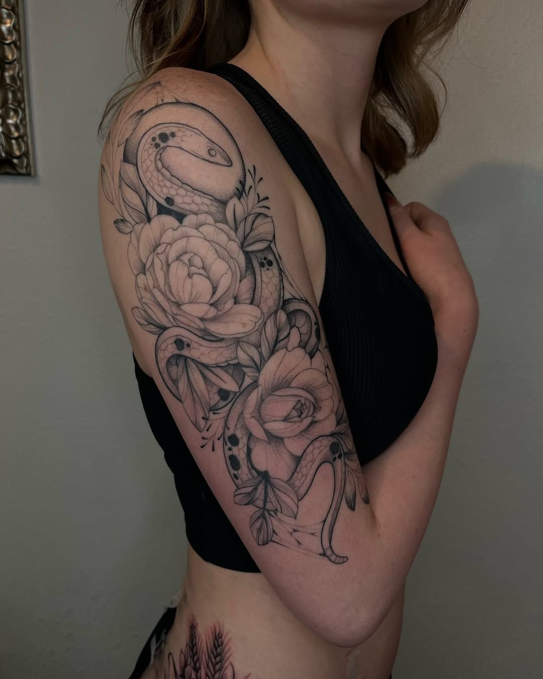 A woman has a snake and roses tattoo on her arm