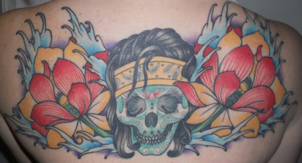 A woman has a tattoo of a skull and flowers on her back