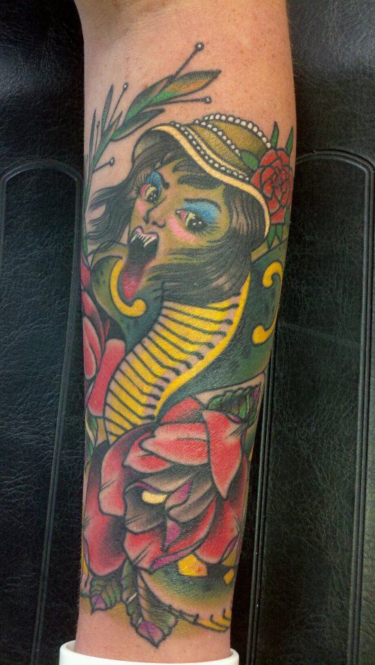 A person has a tattoo of a woman with a snake and flowers on their leg.