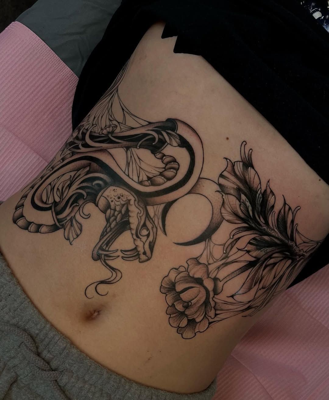A woman has a tattoo of a dragon and flowers on her stomach