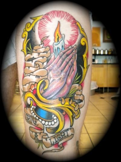 A tattoo of praying hands with a candle and a banner that says