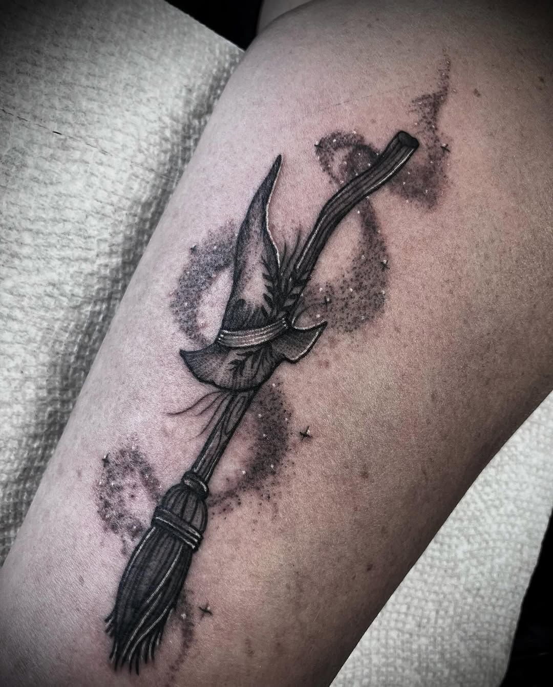 A black and white tattoo of a witch 's broom with a witch 's hat on it.