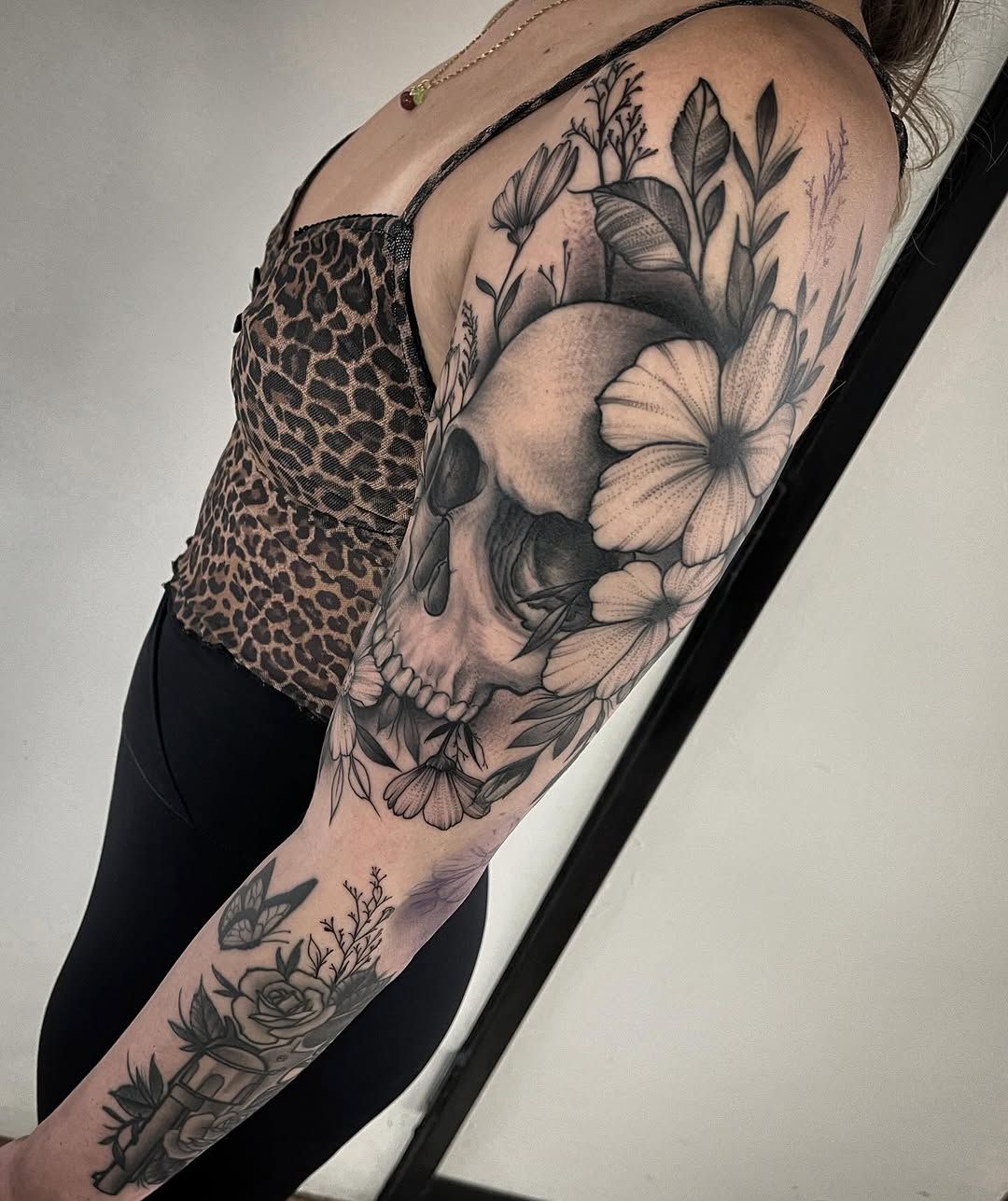 A woman has a tattoo of a skull and flowers on her arm