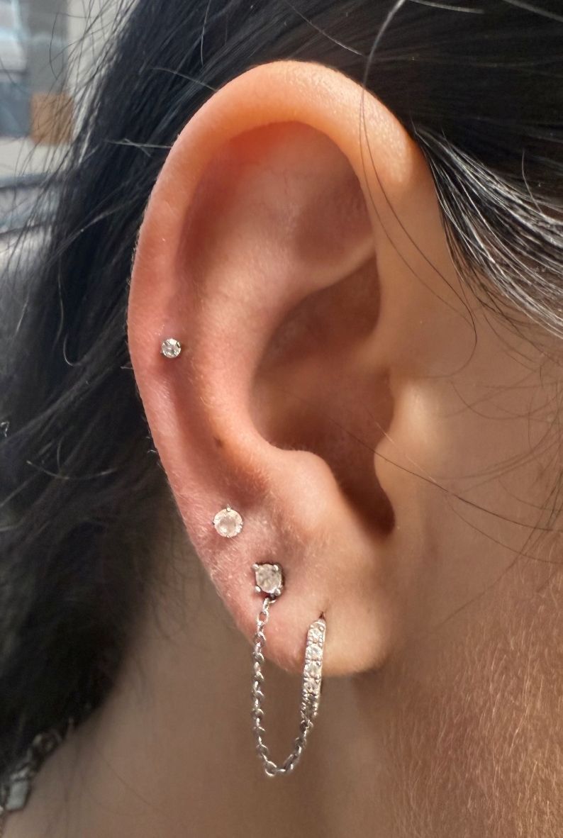 Close-up of a person's ear, showcasing multiple piercings with small, delicate earrings.