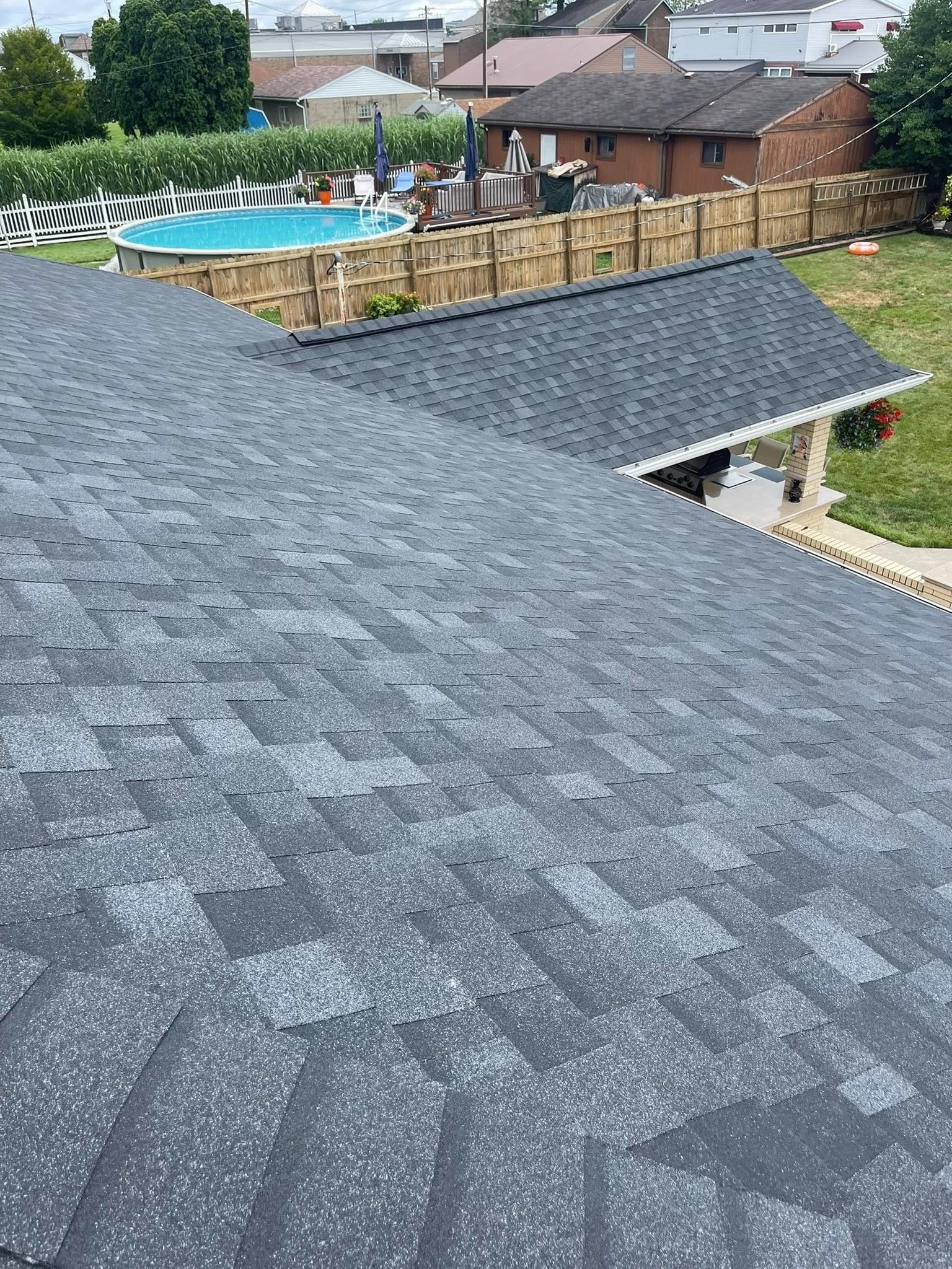 Dark gray shingle roof, angled perspective. A backyard with a pool, fence, and other houses are in the background.
