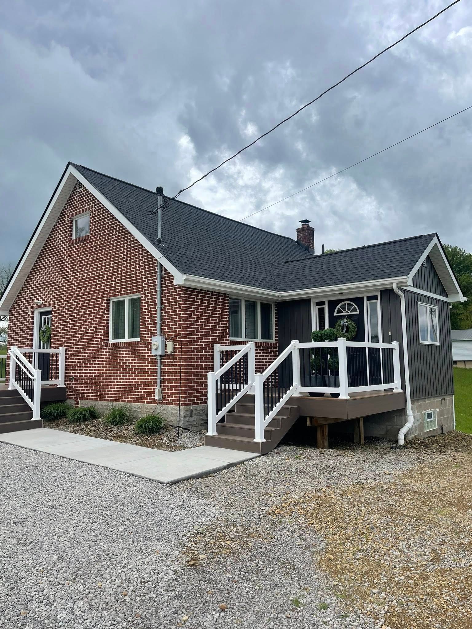 A two-toned house with a red brick section and a gray section, featuring white trim and a dark roof under a cloudy sky.