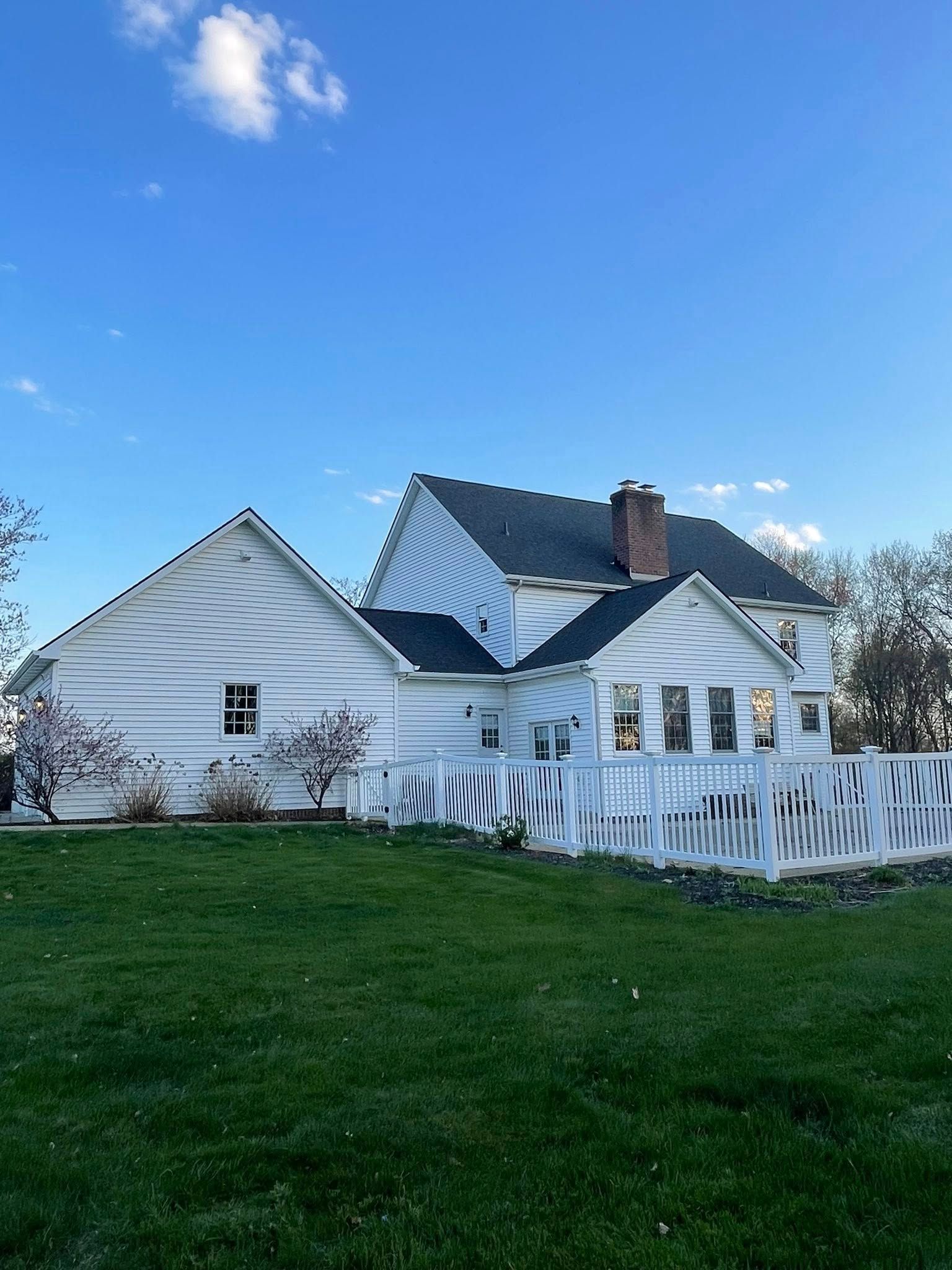 White house with a sloped roof, side building, and picket fence against a blue sky and green grass.