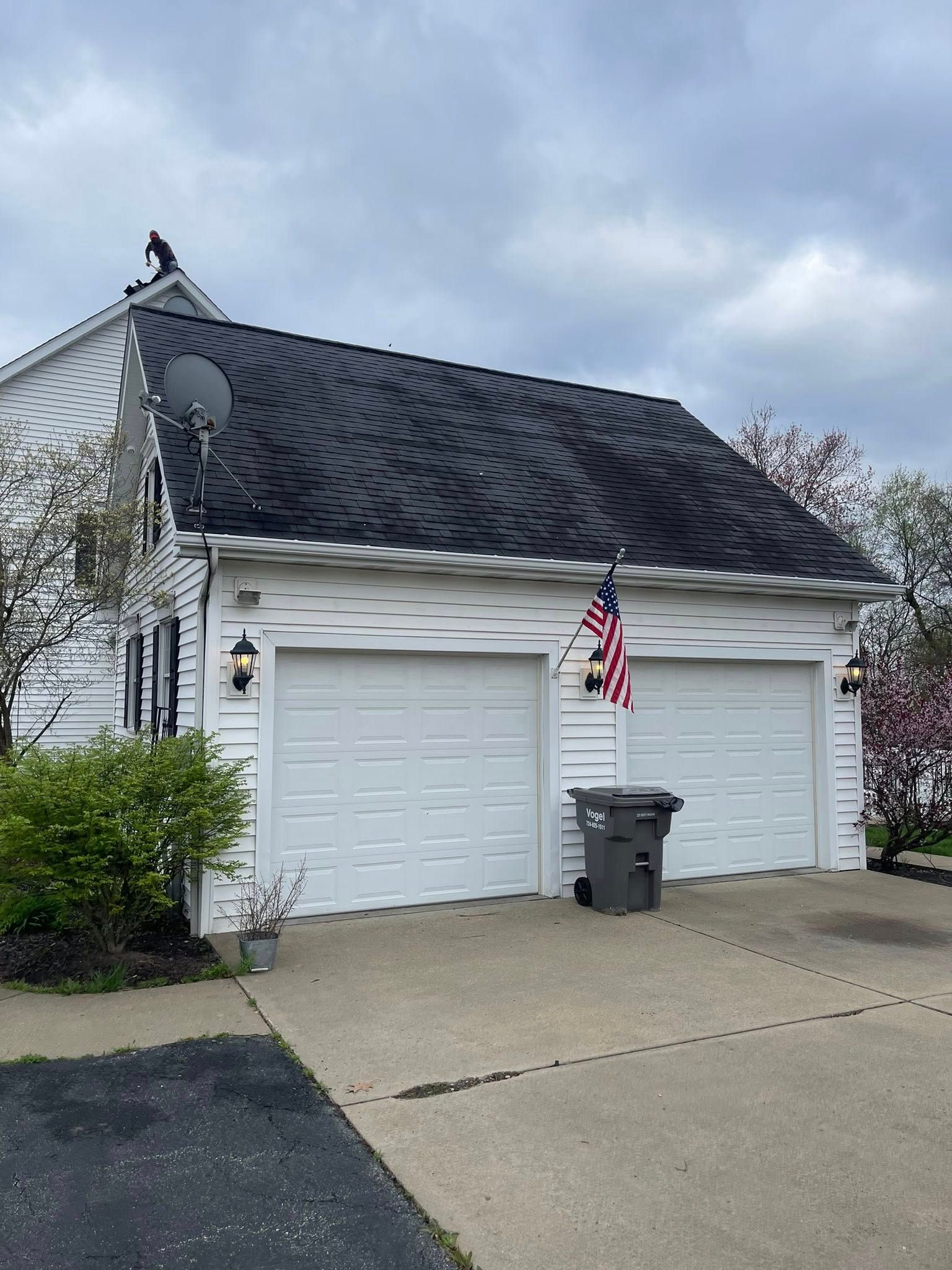White two-car garage with a black roof and American flag in front. An overcast sky is above the house.