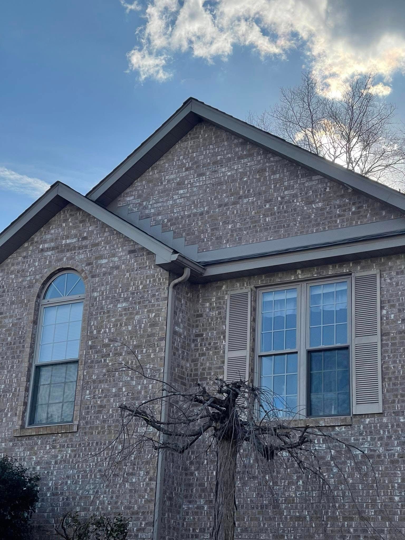 Brick house exterior with an arched window on the left and a rectangular window with shutters on the right; blue sky with clouds.