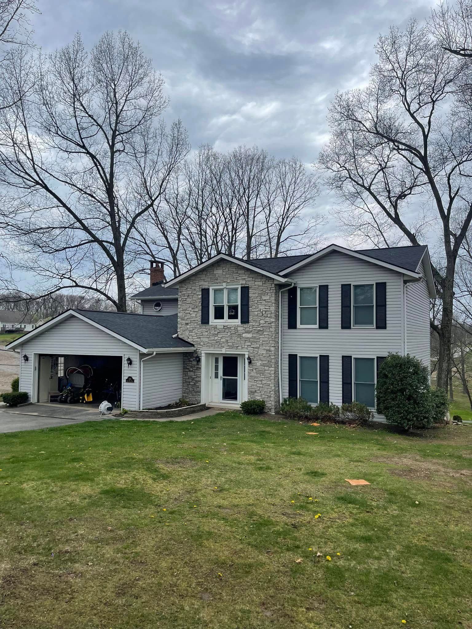 Two-story house with a stone front, attached garage, and black shutters under a cloudy sky. Green lawn in front.