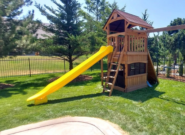 Wooden backyard playset with a bright yellow slide on a green lawn.