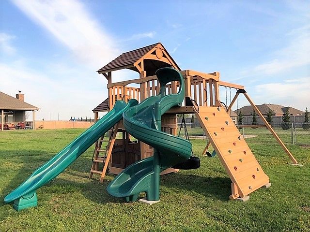 Backyard playset with green slides, tan climbing wall, and wooden tower on grass