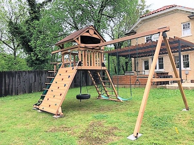 Wooden backyard swing set with slide, climbing wall, and hanging tire in a grassy yard