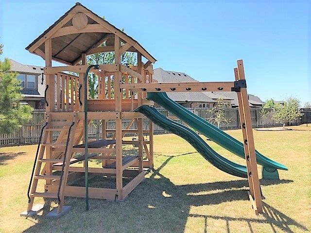 Wooden playground tower with green slides and stairs in a sunny park
