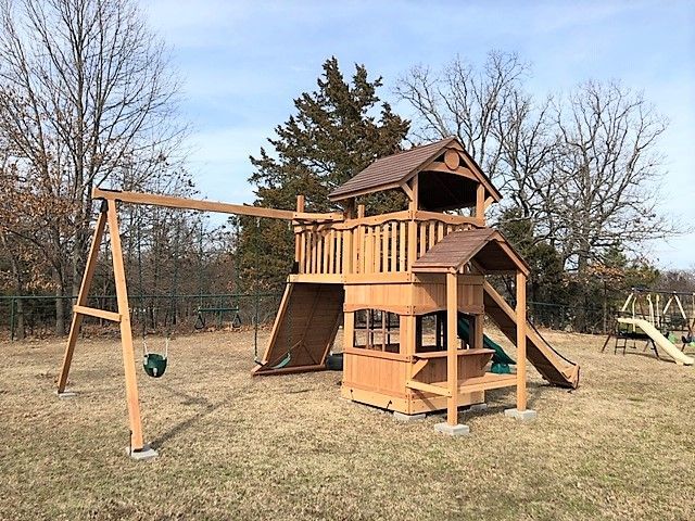 Wooden backyard playset with slide, swing, and tower on a grassy lawn