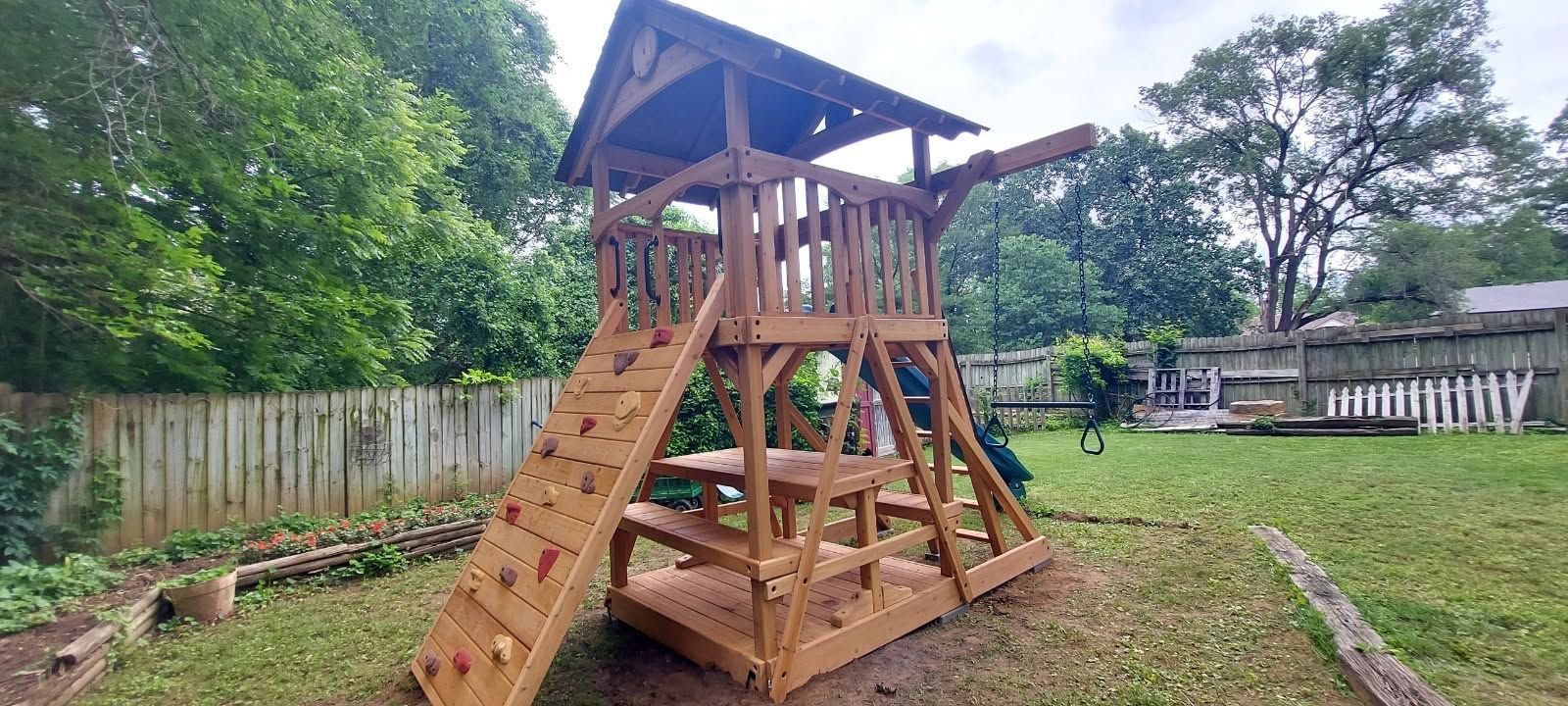 Wooden backyard playground tower with stairs, slide, and roof on a grassy yard