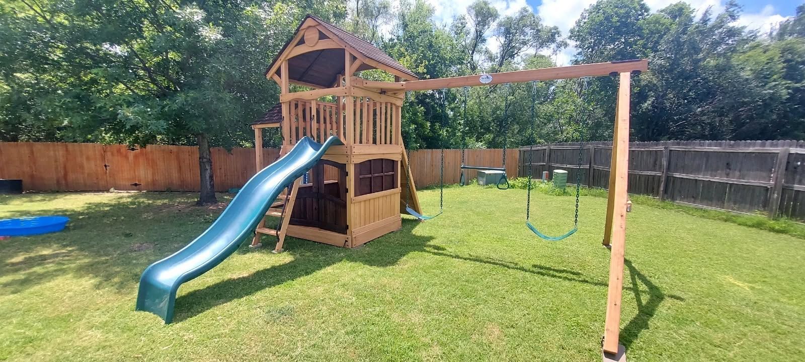 Backyard playset with blue slide, swing, and wooden fort on a sunny lawn