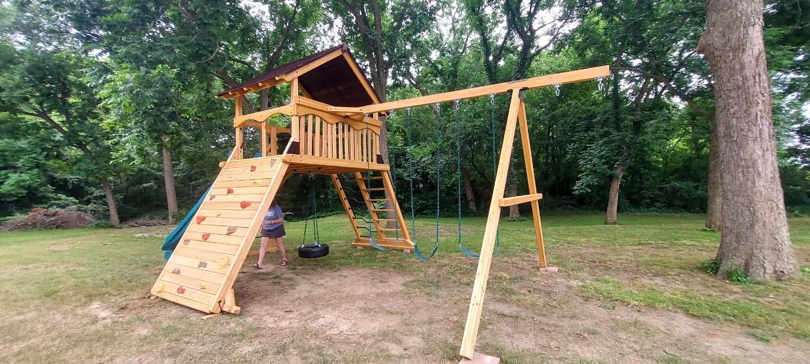 Wooden backyard playground set with slide, swings, and a climbing frame on grass under trees