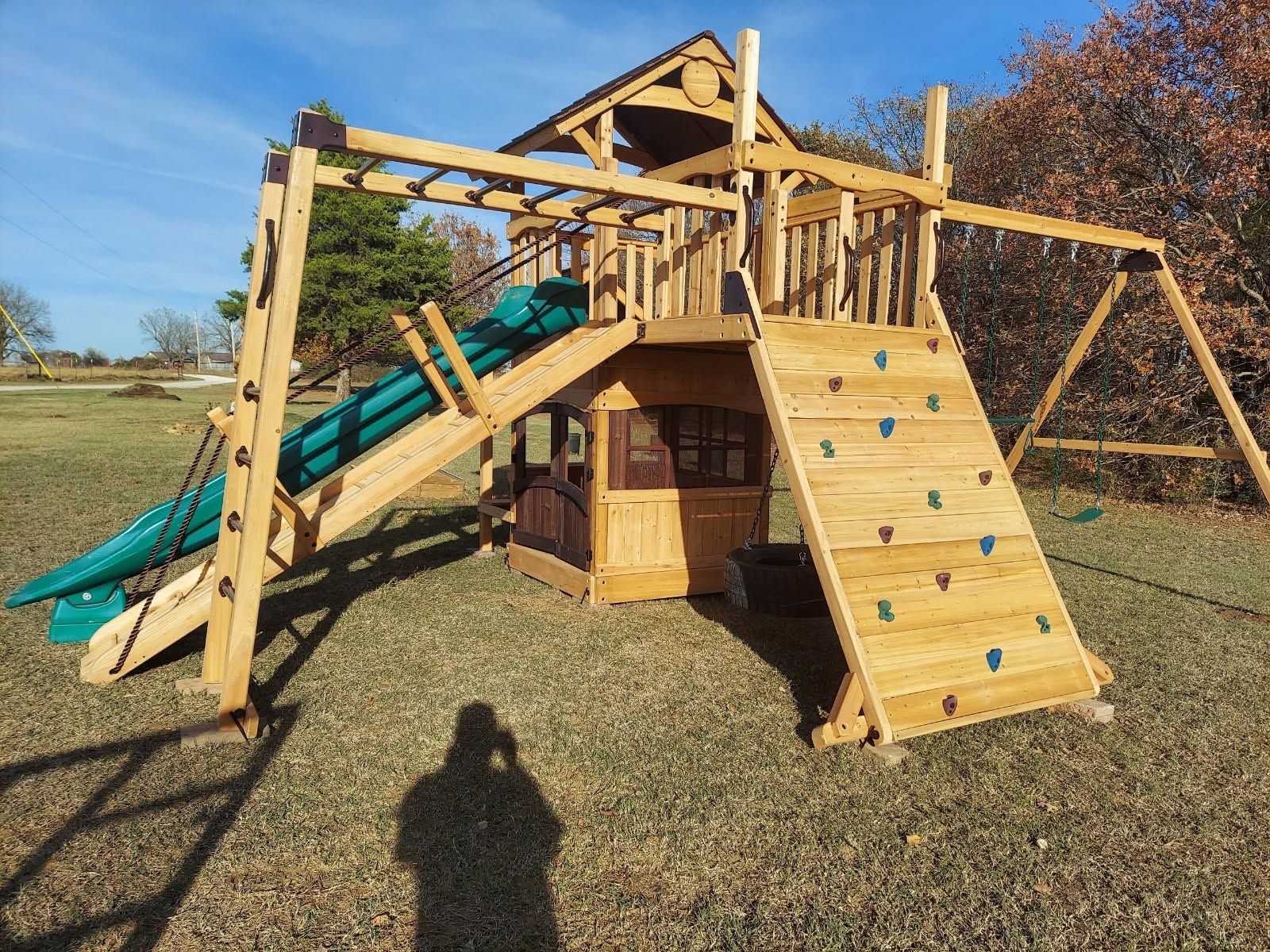 Wooden playground fort with slides, climbing wall, and swing set in a grassy yard