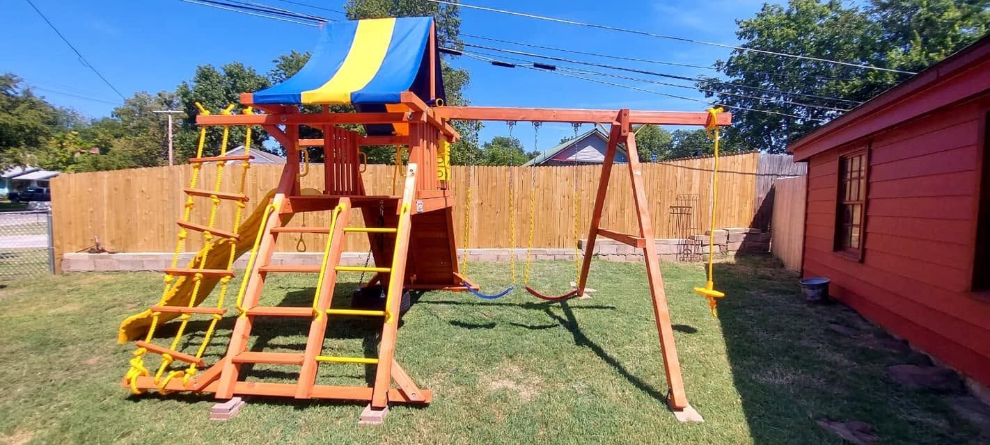 Backyard wooden playset with slide, ladder, and swing next to a red shed and fence