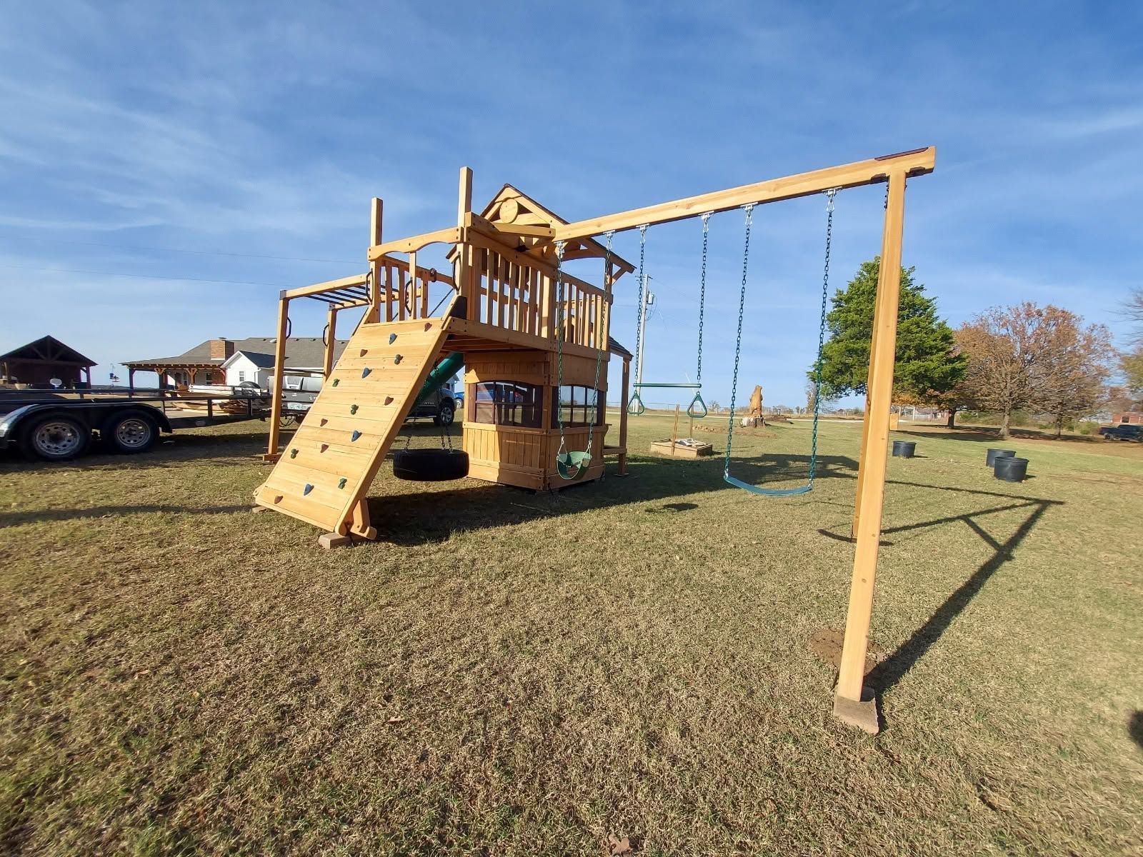 Wooden playground with slide and swing set in a grassy field on a sunny day