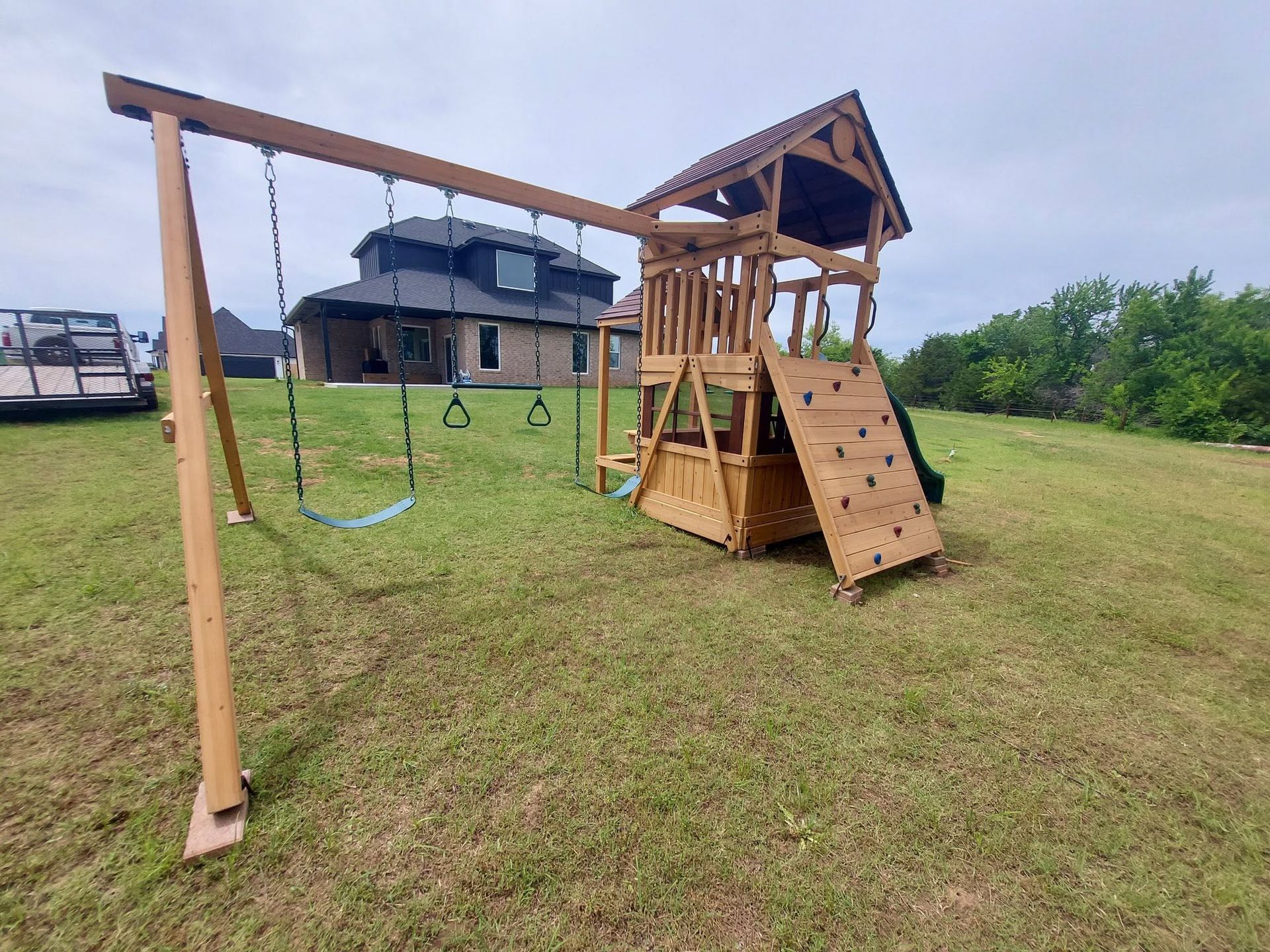 Wooden backyard playset with swings and climbing ladder on a grassy lawn near a house